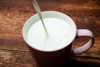 Süt kahverengi ahşap bir arka planda bir fincana dökülür..