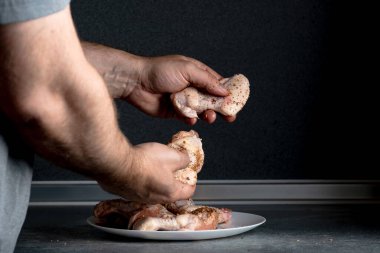 Bir adam tavuk kanatlarını pişirmek için baharatlarla ovalıyor..