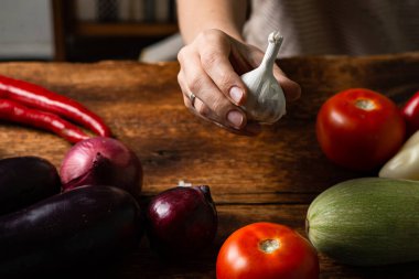 Tahta bir arka planda farklı sebzelerle bir kadın elinde çiğ sarımsak..