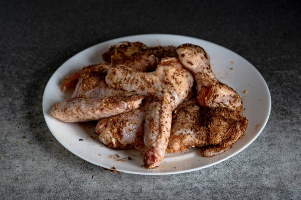 Rohe Hühnerflügel Mit Gewürzen Auf Einem Weißen Teller Vor Dunklem — Stockfoto