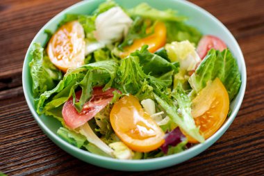 Tahta arka planda taze sebzelerden, otlardan ve domateslerden oluşan sağlıklı bir salata.