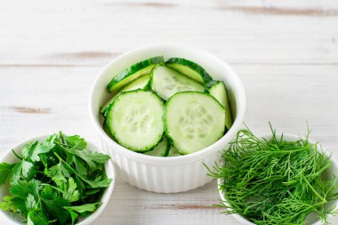 Taze doğranmış salatalık, maydanoz, beyaz ahşap arka planda dereotu. Salata malzemeleri. Vejetaryen gıda konsepti.