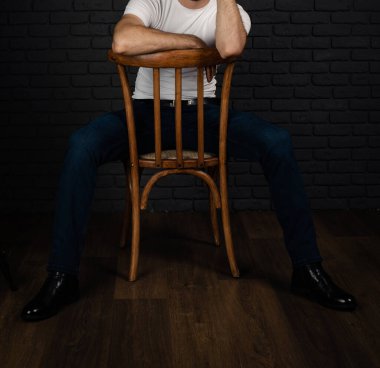 Beyaz tişörtlü, kolunda saati olan tanınmamış bir adam sandalyede oturuyor..