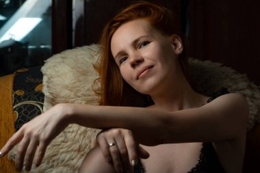 Orta yaşlı, 40 yaşında, kızıl saçlı, karanlık bir odada oturan bir kadın.