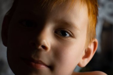 Karanlık bir odada genç kızıl saçlı bir çocuğun portresi.