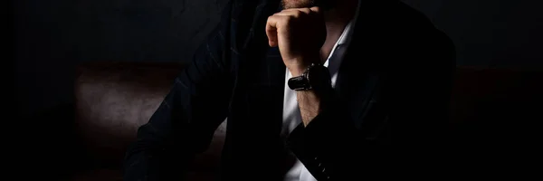 Tarz sahibi kıyafetleri içinde tanınmayan bir adam karanlıkta kanepede rahatça oturur..