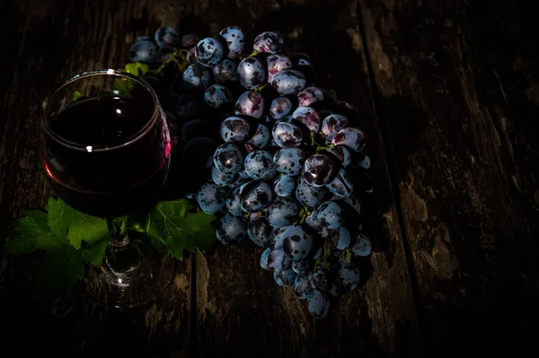 Grapes on a old wooden table and a glass of red wine — Stock Photo, Image