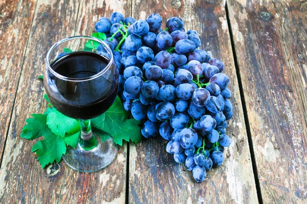 Grapes on a old wooden table and a glass of red wine — Stock Photo, Image