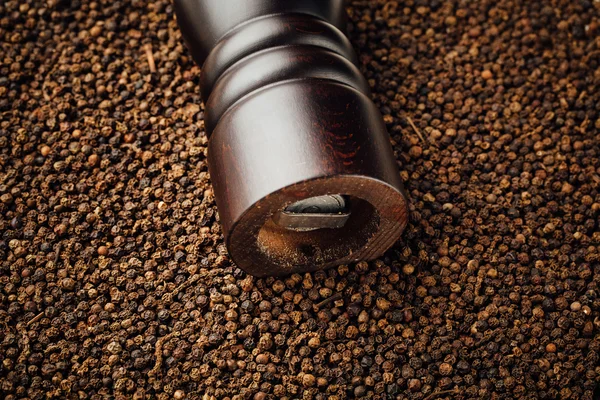 Pepper mill on peppercorns background — Stock Photo, Image
