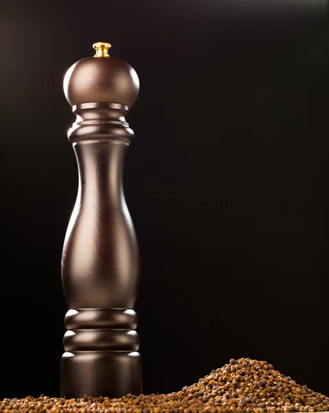 Pepper mill and peppercorns heap, black background — Stock Photo, Image