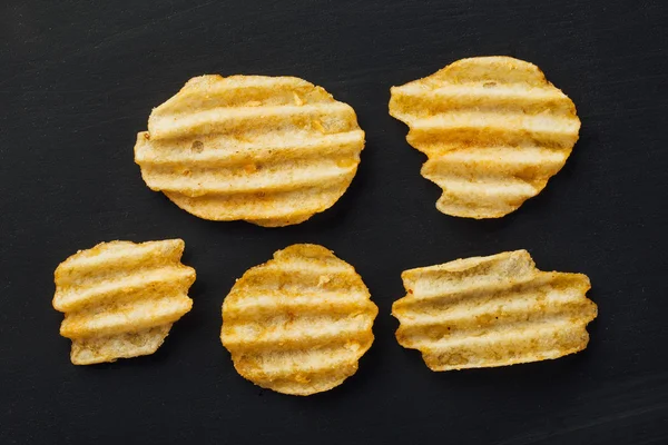 Wellige Kartoffelchips auf schwarzem Hintergrund — Stockfoto