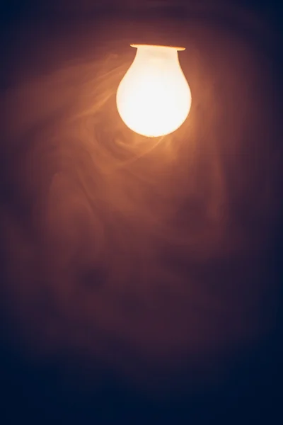 Bulb lamp warm light in smoke — Stock Photo, Image