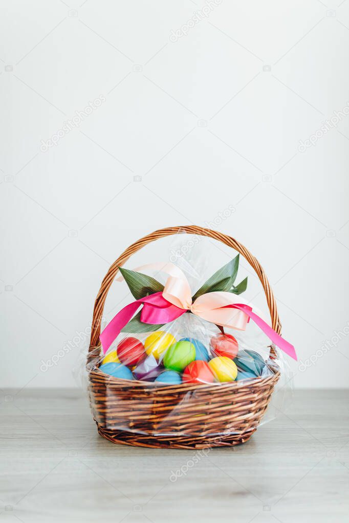 Easter color eggs in festive gift basket, light gray wooden background with copy-space