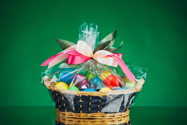 Easter gift basket with multicolor eggs, green background