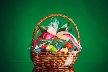Renkli yumurtaları ve yeşil arka planı olan neşeli Paskalya sepeti.