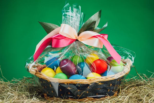 Easter gift basket with multicolor eggs, green background