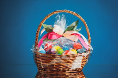 Çok renkli yumurtalı Paskalya hediyesi sepeti, mavi arka plan.