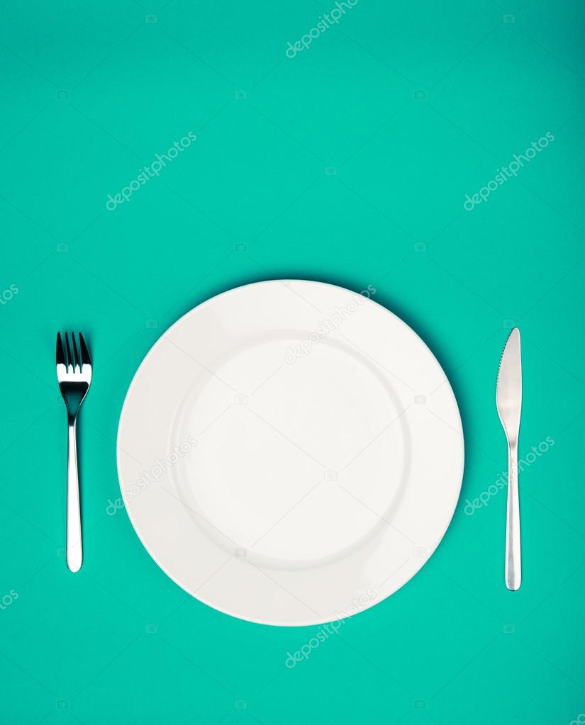 white plate, fork and knife on emerald background