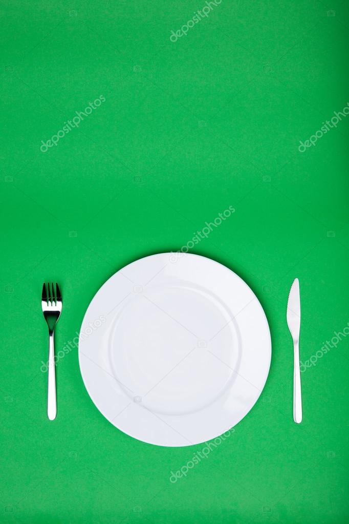 white plate, fork and knife on green background