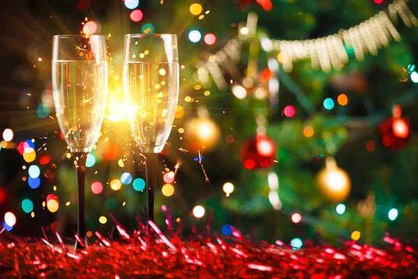 Pair of champagne glasses and sparkler, Christmas tree ornament as the background — Stock Photo, Image