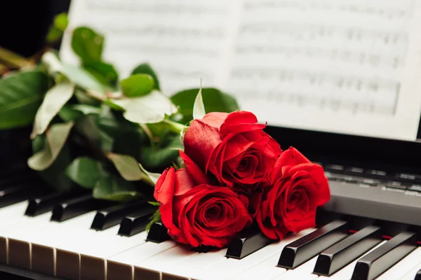 Rose rosse sui tasti del pianoforte e libro di musica — Foto Stock