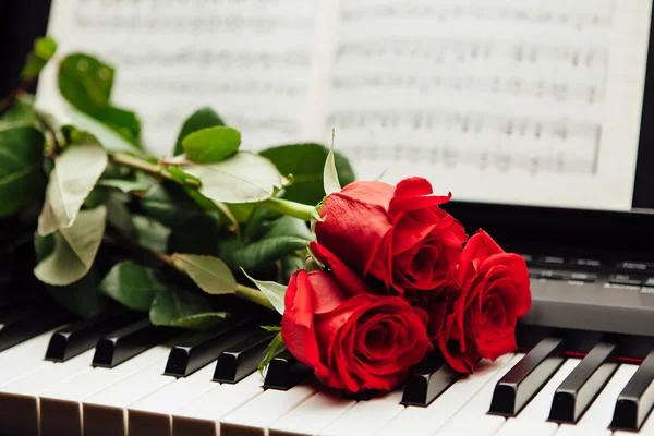 Rosas rojas en teclas de piano y libro de música Imagen de archivo