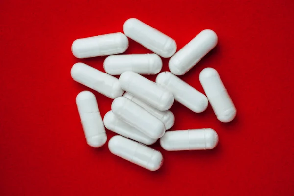 Cápsulas blancas píldoras sobre fondo rojo — Foto de Stock