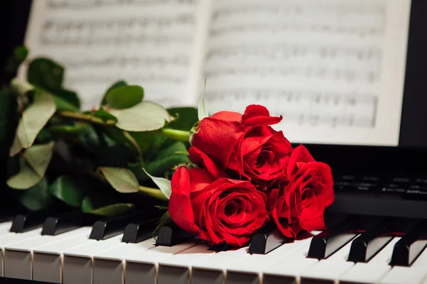 Rose rosse sui tasti del pianoforte e libro di musica — Foto Stock