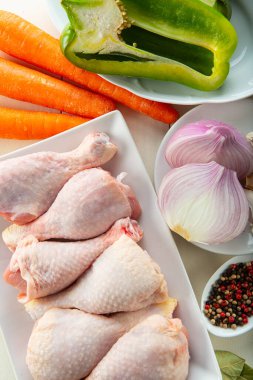 Mutfak masasında pişirmek için çiğ tavuk budu ve sebze.