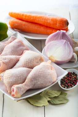 Mutfak masasında pişirmek için çiğ tavuk budu ve sebze.