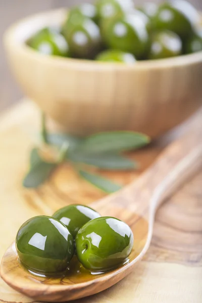 Tigela de madeira e colher com azeitonas verdes e azeite — Fotografia de Stock