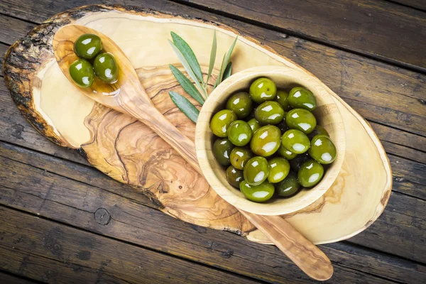 Wooden bowl and spoon with green olives and olive oil — Stock Photo, Image