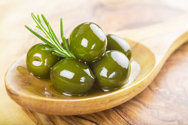 Closeup from green olives with oil on a wooden spoon