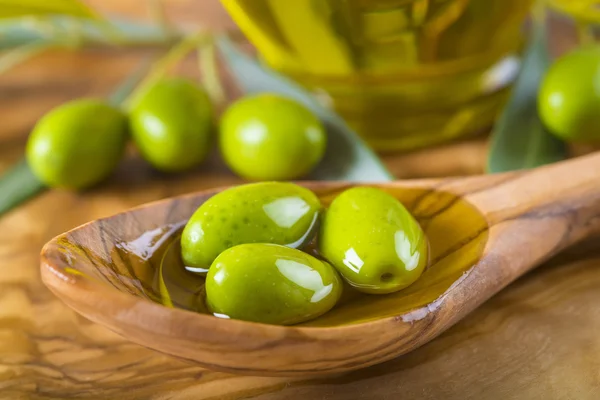 Green olives and oil on a wooden spoon — Stock Photo, Image