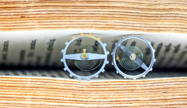 Zahnräder aus einem Uhrwerk unter den alten Buchseiten — Stockfoto
