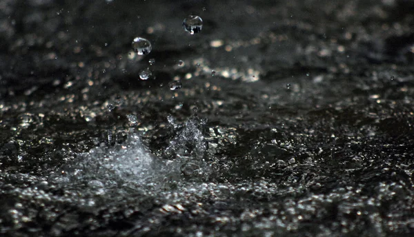 Gotas de agua levitando en el aire en la oscuridad. El agua salpicando vuela en el aire. Parte de las gotas está en foco, parte fuera del foco . — Foto de Stock