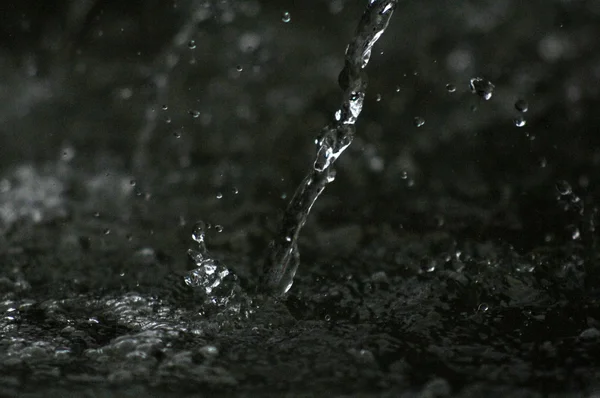 Gotas de agua levitando en el aire en la oscuridad. El agua salpicando vuela en el aire. Parte de las gotas está en foco, parte fuera del foco . — Foto de Stock
