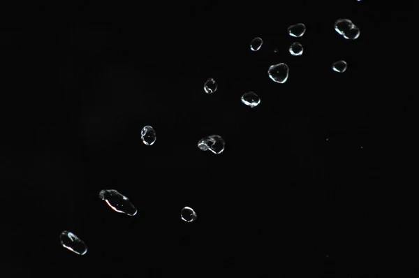 A água cai levitando no ar no escuro. Salpicos de água voam no ar. Parte das gotas está em foco, parte - fora do foco . — Fotografia de Stock