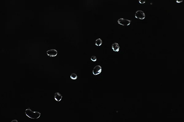 Wassertropfen schweben im Dunkeln in der Luft. Spritzwasser fliegt durch die Luft. Teil der Tropfen steht im Fokus, Teil - aus dem Fokus. — Stockfoto