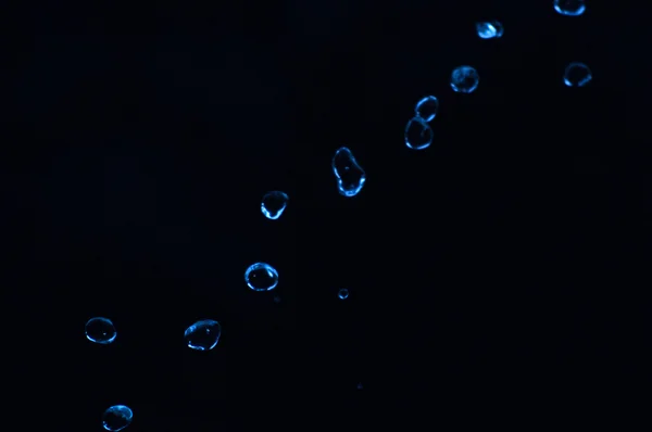 Wassertropfen schweben im Dunkeln in der Luft. Spritzwasser fliegt durch die Luft. Teil der Tropfen steht im Fokus, Teil - aus dem Fokus. — Stockfoto