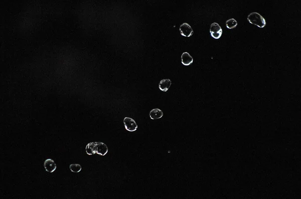 A água cai levitando no ar no escuro. Salpicos de água voam no ar. Parte das gotas está em foco, parte - fora do foco . — Fotografia de Stock