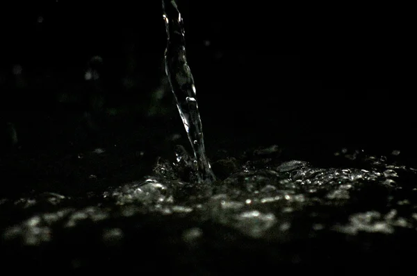 Wasser strömt die Luft im Dunkeln. Spritzwasser fliegt durch die Luft. Teil der Tropfen steht im Fokus, Teil - aus dem Fokus. — Stockfoto