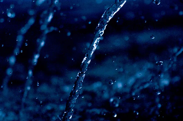 Water stream the air in dark. Splashing water fly in the air. Part of the drops is in focus, part - out of the focus. — Stock Photo, Image