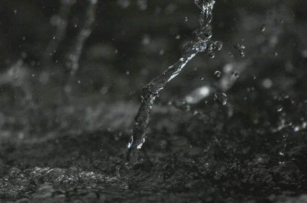 Vattenströmmen luften i mörkret. Stänkande vatten flyger i luften. Del av dropparna är i fokus, del - av fokus. — Stockfoto
