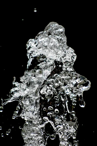 A água cai levitando no ar no escuro. Salpicos de água voam no ar. Parte das gotas está em foco, parte - fora do foco . — Fotografia de Stock