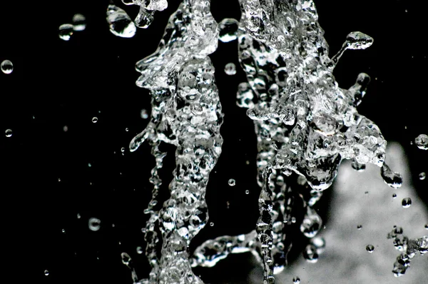 A água cai levitando no ar no escuro. Salpicos de água voam no ar. Parte das gotas está em foco, parte - fora do foco . — Fotografia de Stock