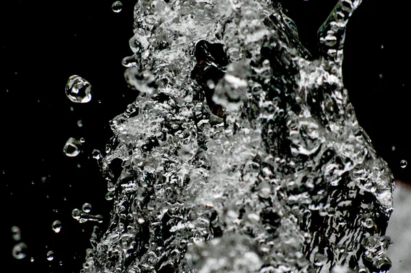 A água cai levitando no ar no escuro. Salpicos de água voam no ar. Parte das gotas está em foco, parte - fora do foco . — Fotografia de Stock