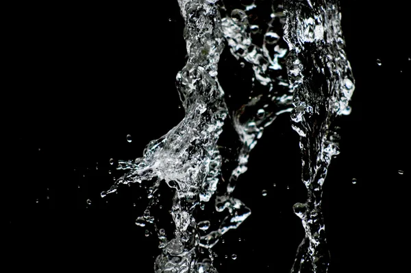 Vatten droppar svävar i luften i mörkret. Stänkande vatten flyger i luften. Del av dropparna är i fokus, del - av fokus. — Stockfoto
