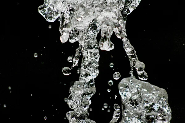 A água cai levitando no ar no escuro. Salpicos de água voam no ar. Parte das gotas está em foco, parte - fora do foco . — Fotografia de Stock