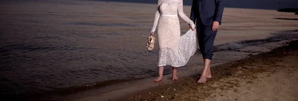 新郎新娘日落时在海滩边散步 — 图库照片